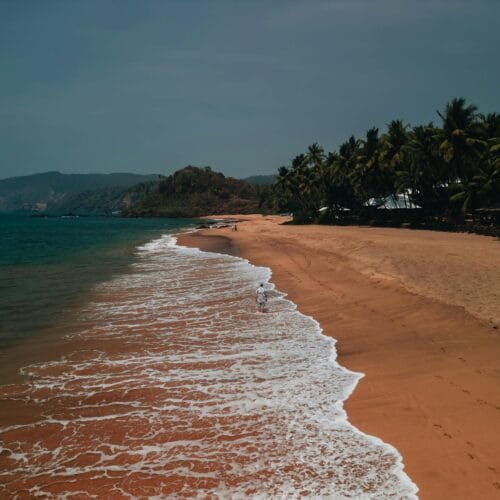 A picturesque aerial view of a serene beach in Goa with golden sands and gentle waves during sunset.